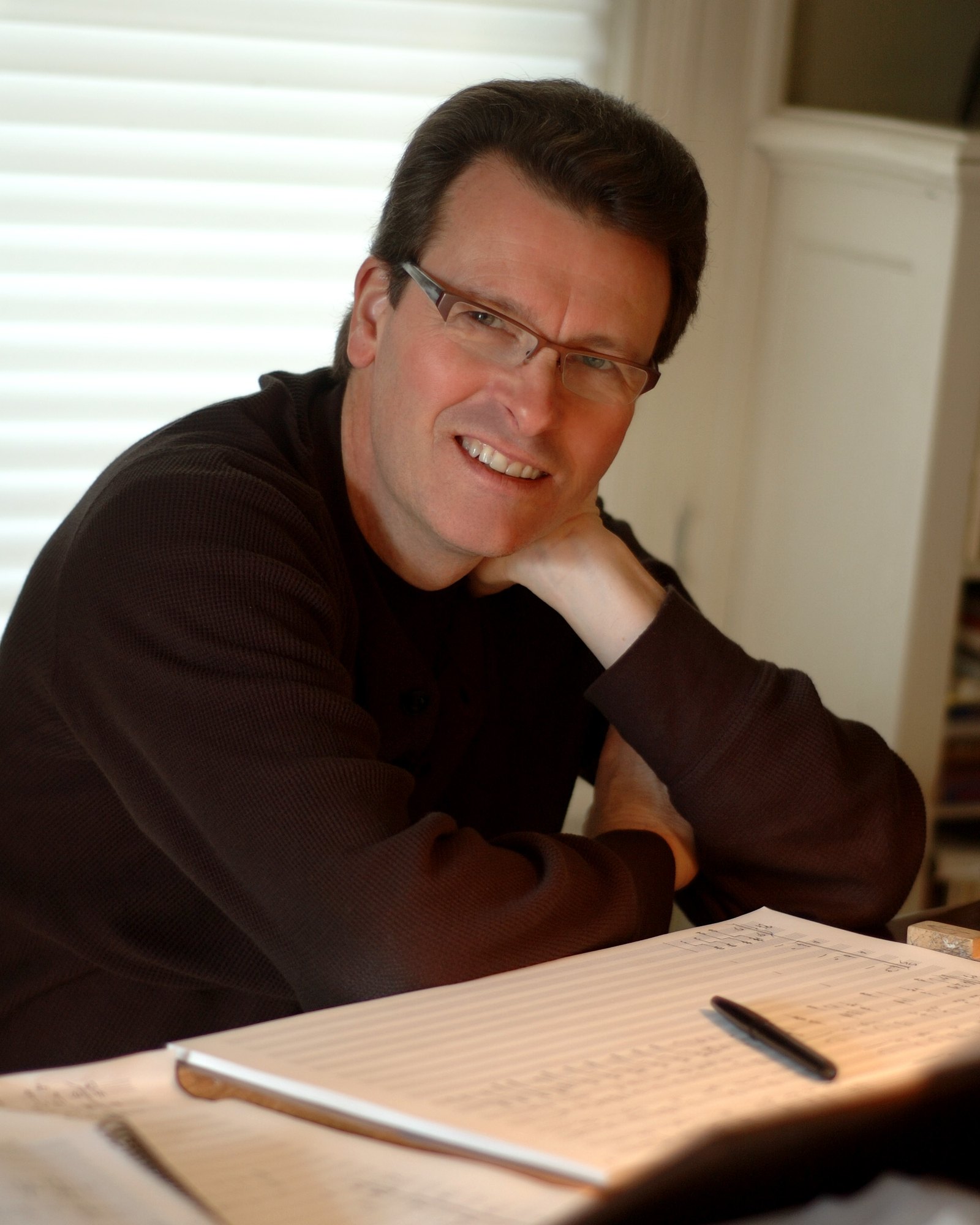 Stephen Paulus at his desk, smiling, with manuscript paper in front of him